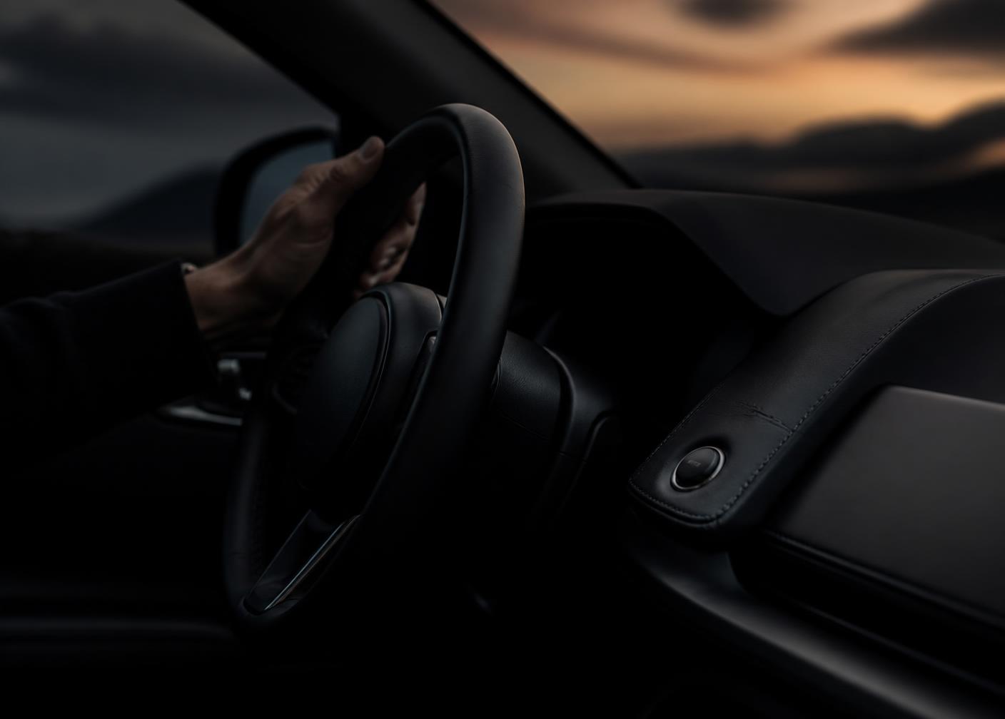 Driver's hand on the steering wheel of a premium car interior at dusk